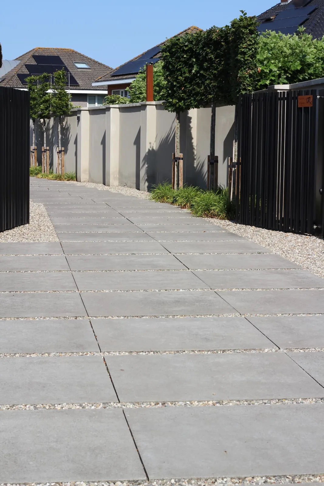 Pad in grootformaat betontegels met grindvoegen langs een strakke tuinmuur