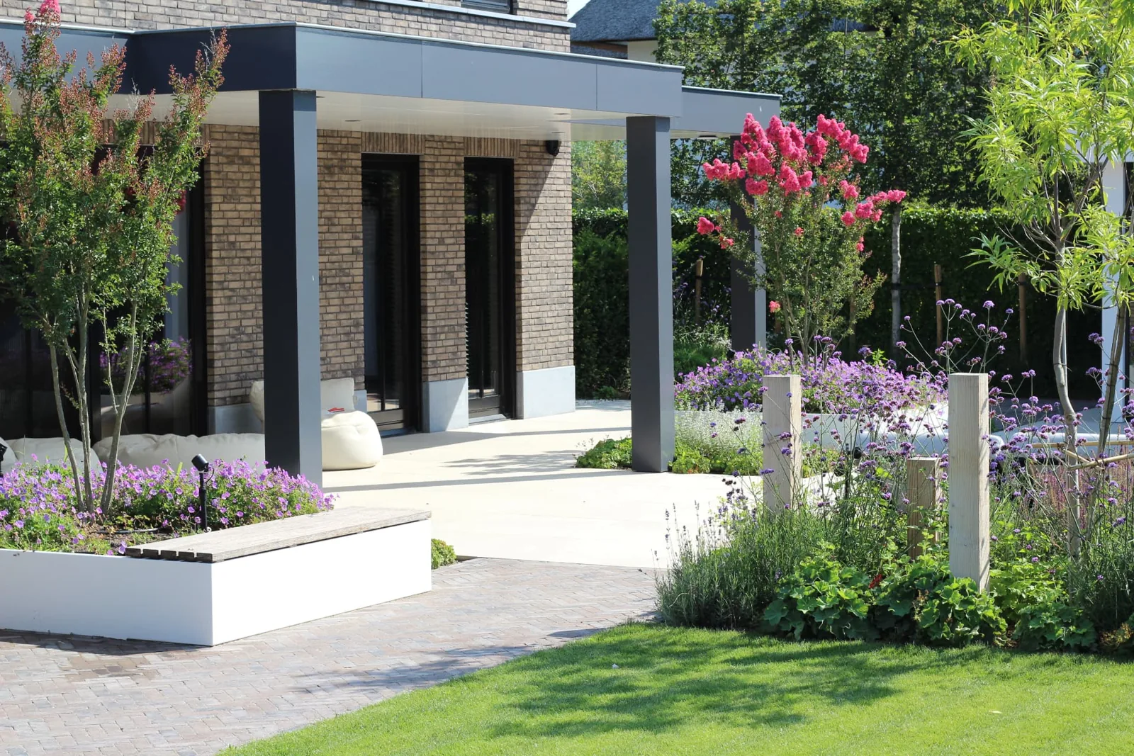 Ruim terras onder een moderne overkapping met witte plantenbakken en een klinkerpad