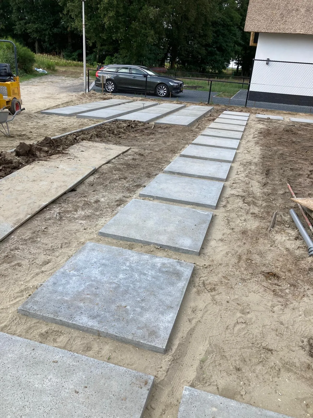 Grondwerk met uitgelegde betonplaten en stapstenen voor een nieuwe oprit