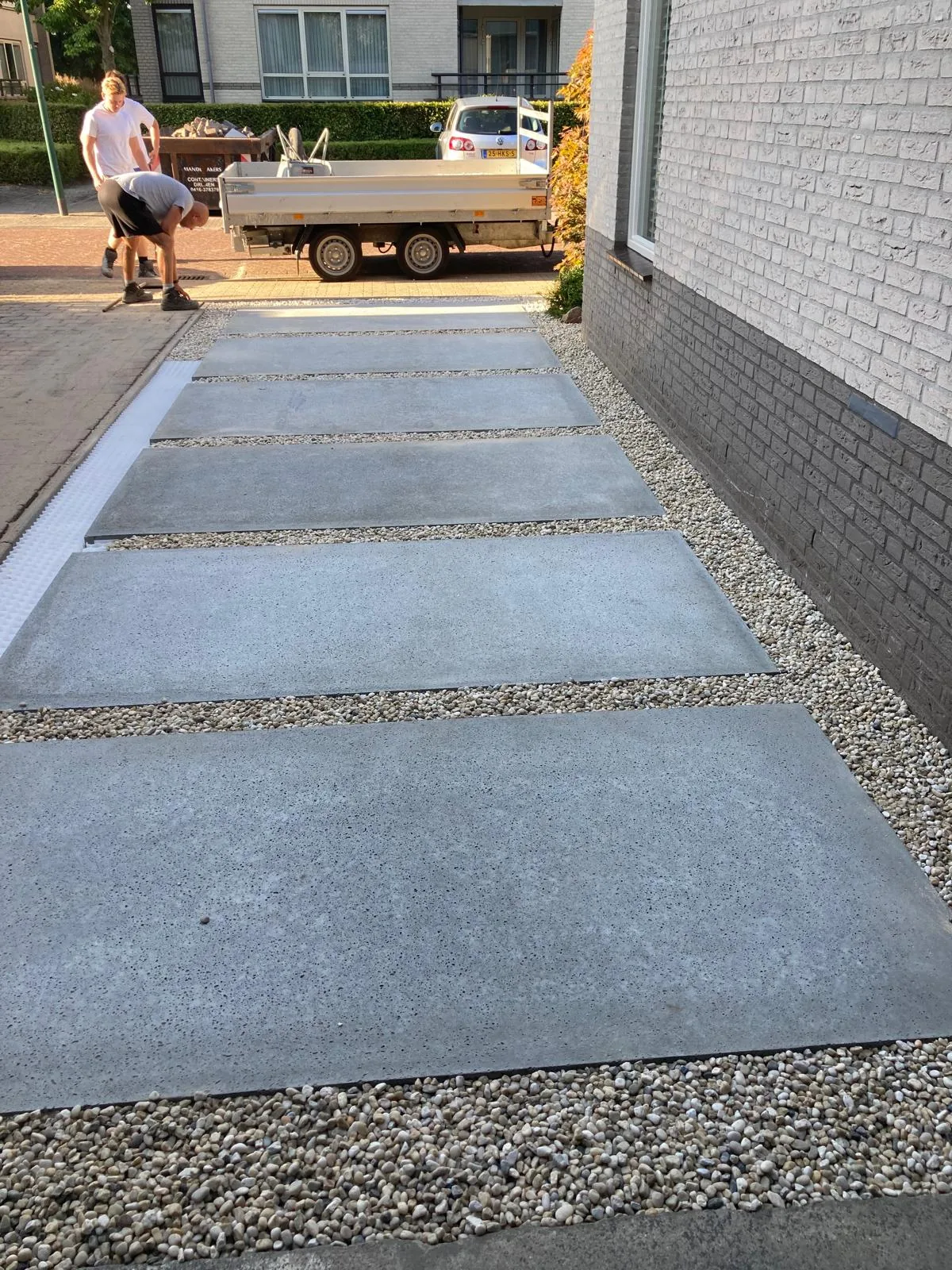 Zijpad in grote betonplaten met siergrind langs een woning, tijdens de aanleg