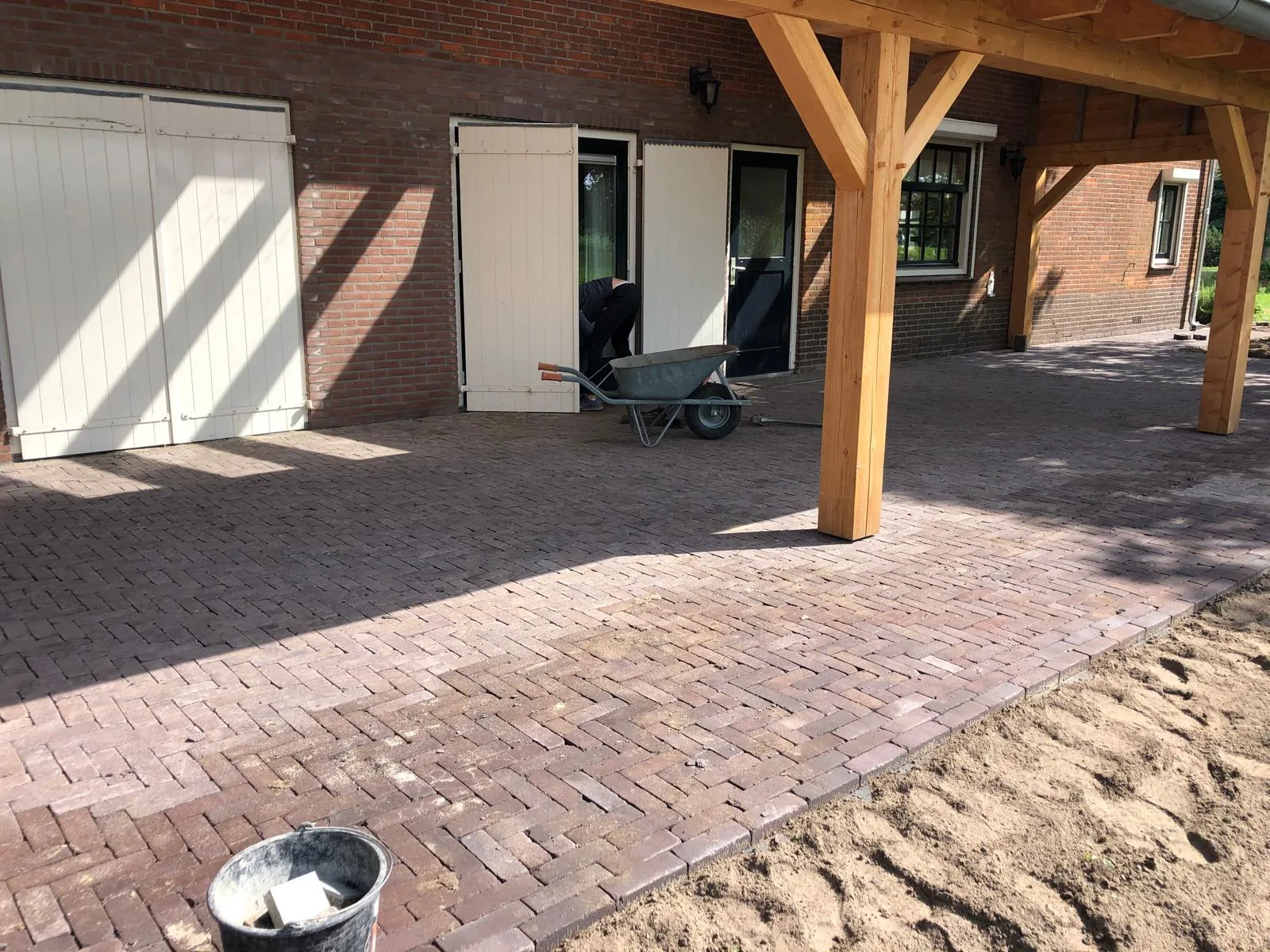 Erf in gebakken klinkers onder een houten overkapping tijdens de uitvoering