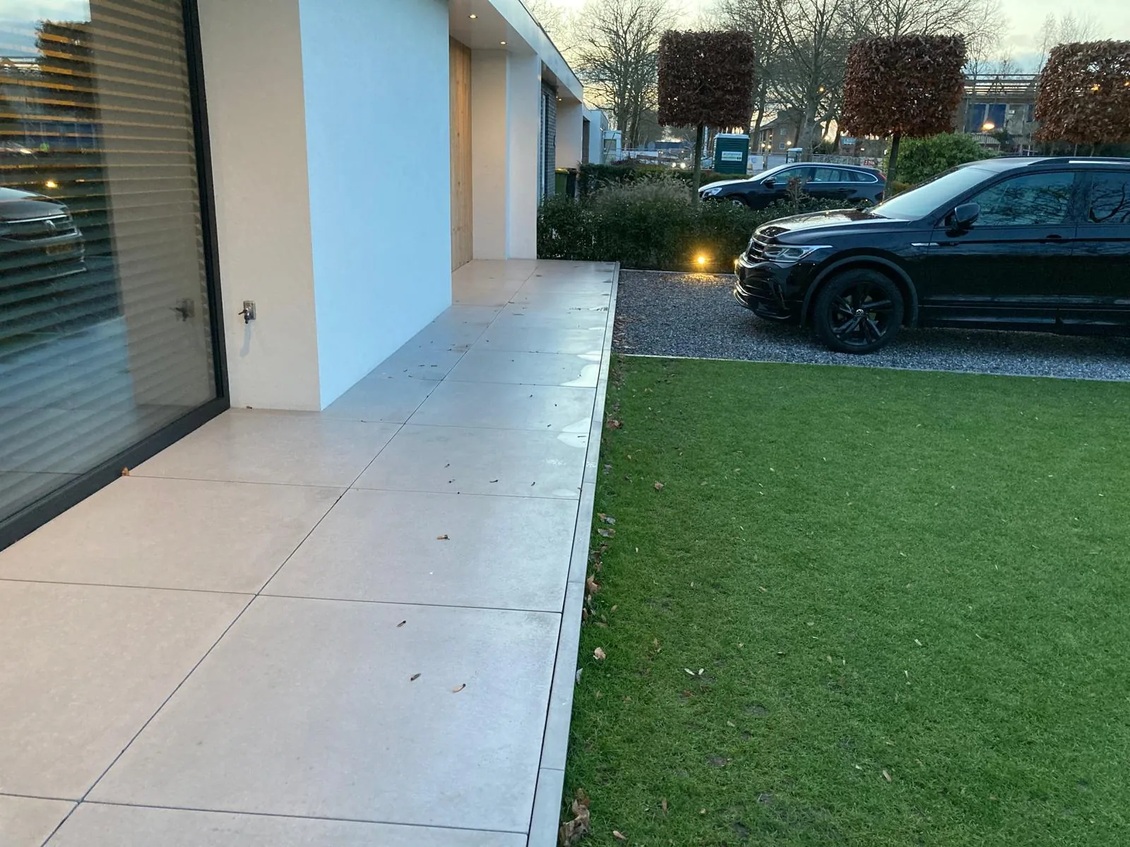 Keramisch terras in lichte tegels langs een moderne woning met kunstgras