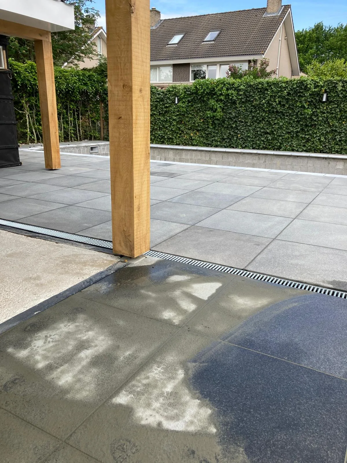 Keramisch terras met lijngoot en houten overkapping bij een nieuwbouwwoning