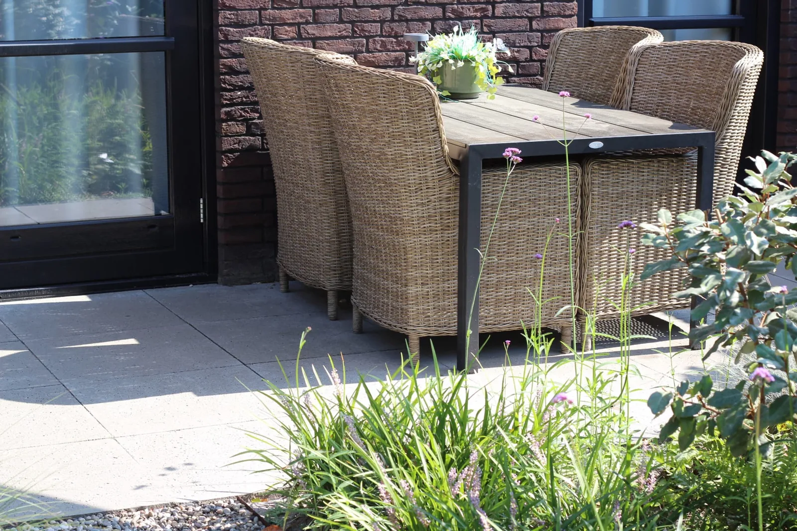 Terras in grootformaat betontegels met tuinmeubilair en beplante borders