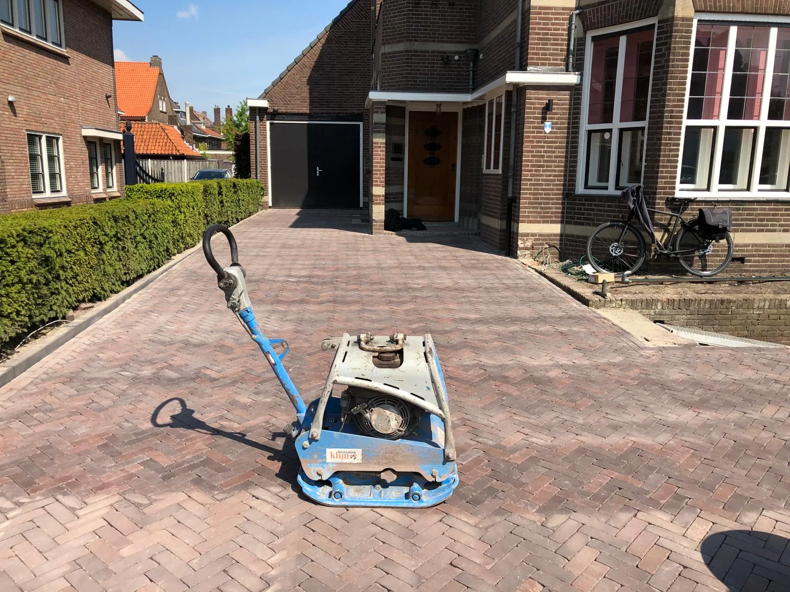 Oprit in gebakken klinkers met trilplaat tijdens de afwerking