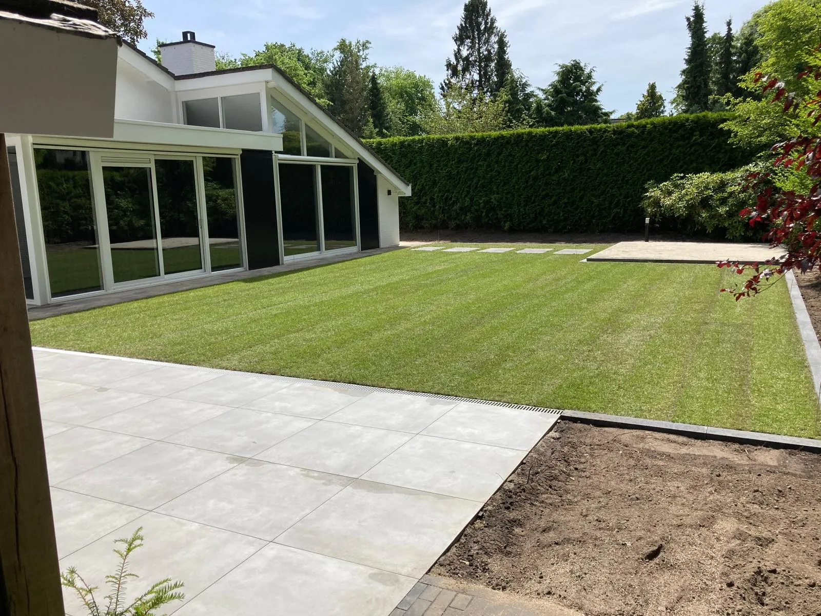 Licht keramisch terras met lijngoot en strak gemaaid gazon in een ruime achtertuin