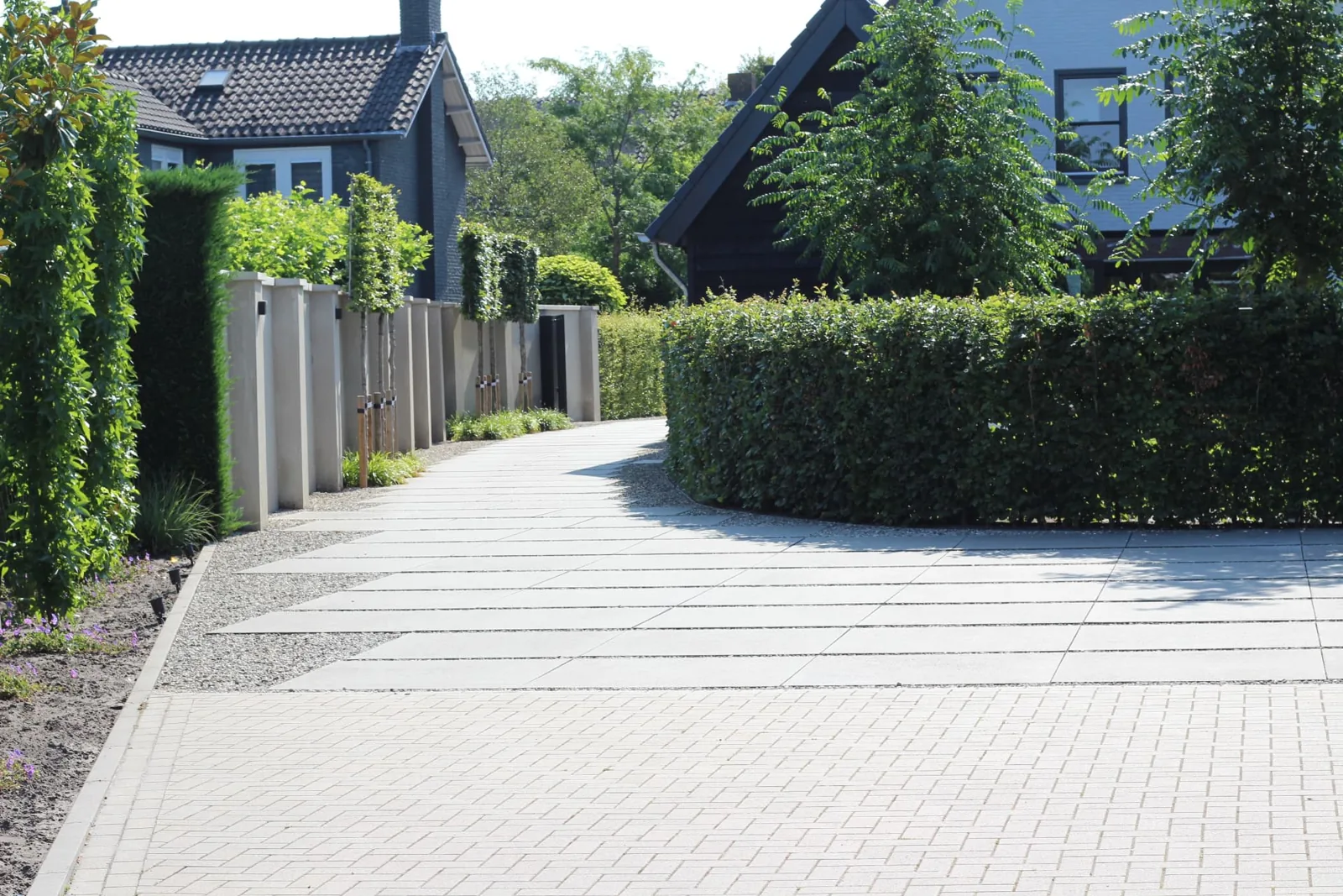 Oprit met een combinatie van grootformaat tegels en lichte klinkers bij een moderne woning