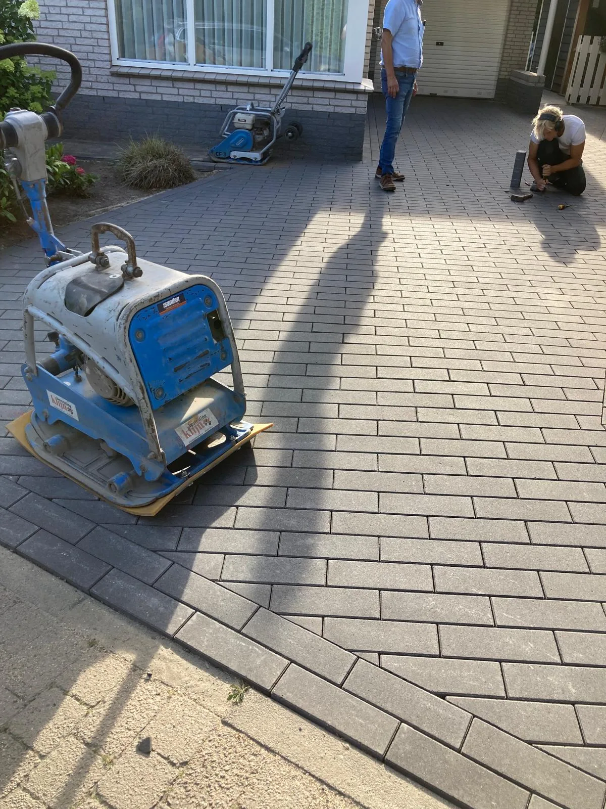 Bestraters van Klijn Bestrating werken een oprit in betonklinkers af met de trilplaat