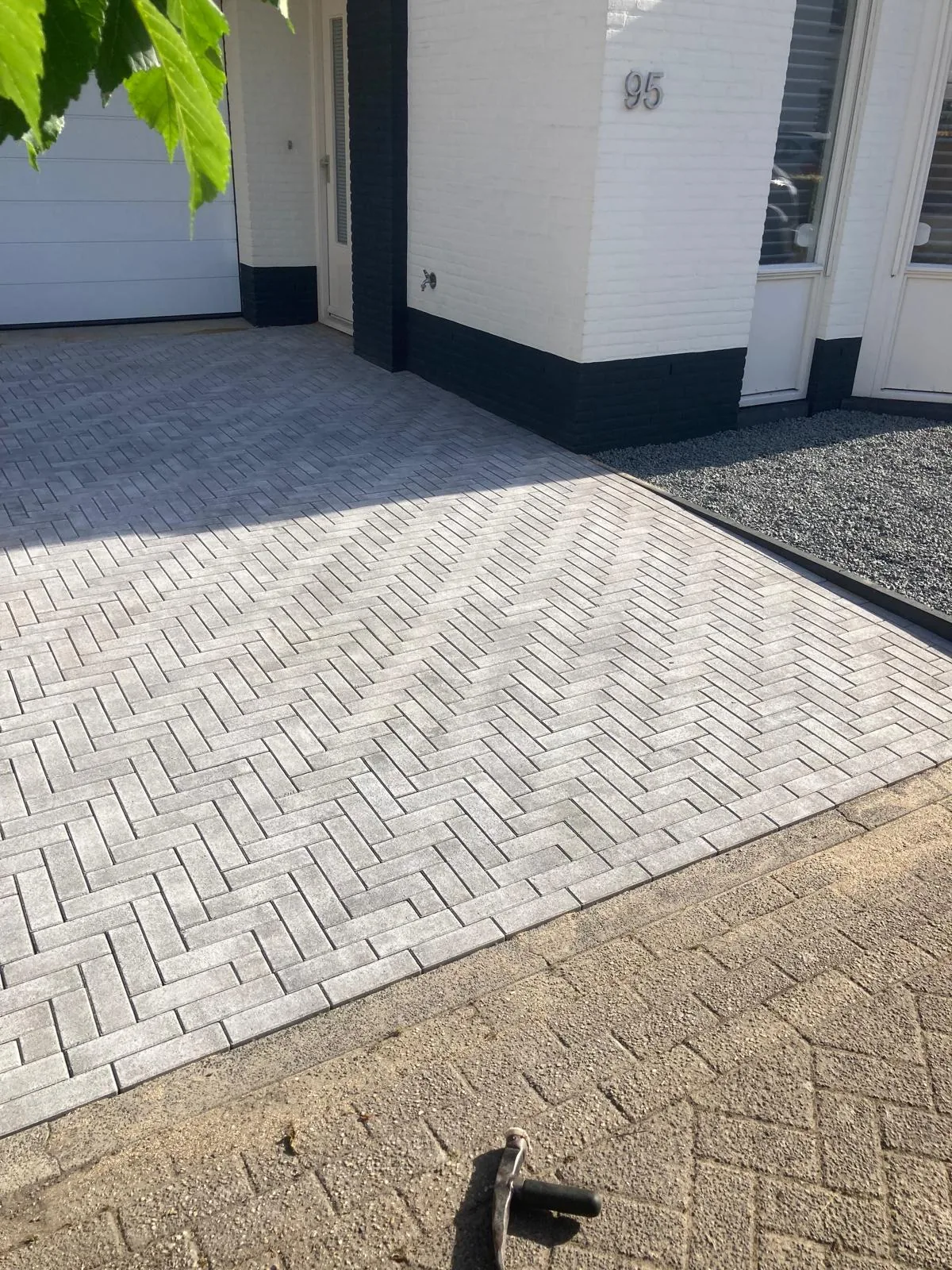 Oprit in grijze betonklinkers in elleboogverband bij een witte woning