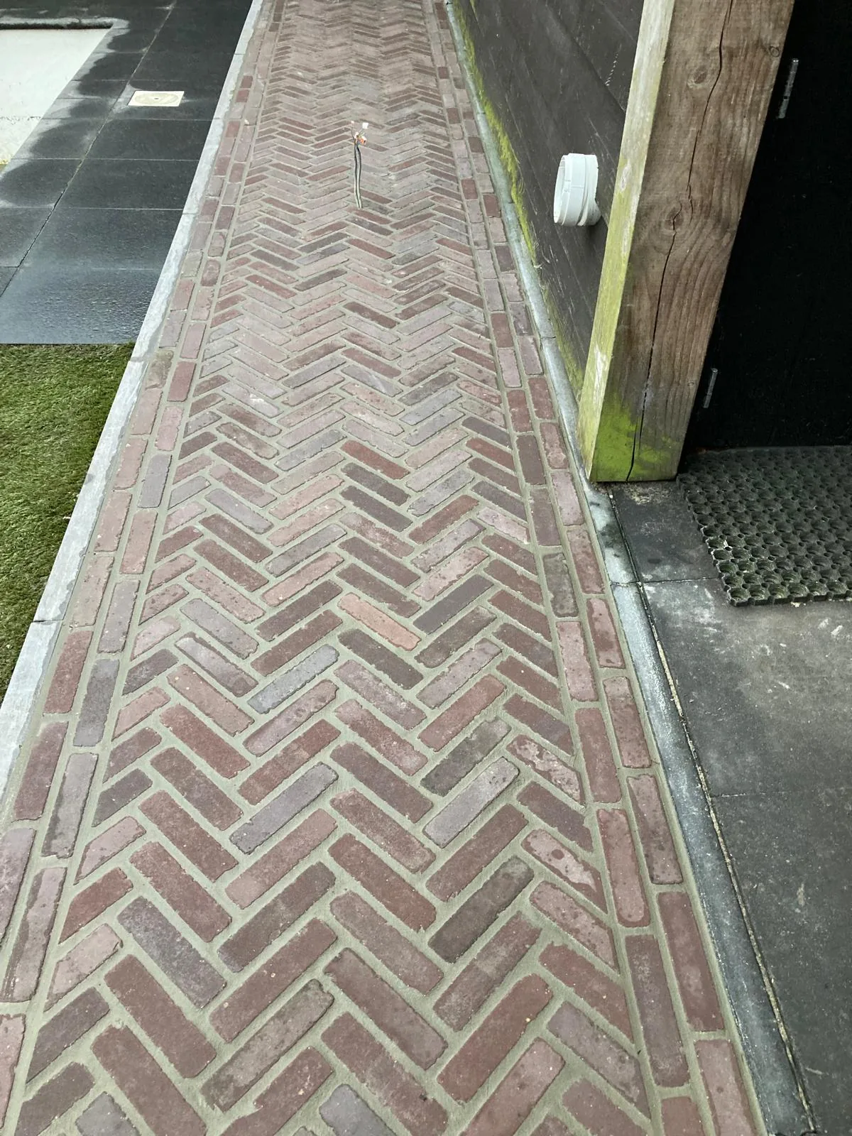 Smal tuinpad in gebakken klinkers in visgraatverband met natuurstenen band