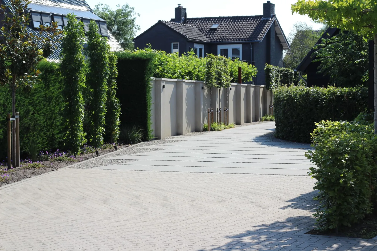 Brede oprit met tegelbanen in beton en klinkerverharding langs muurelementen